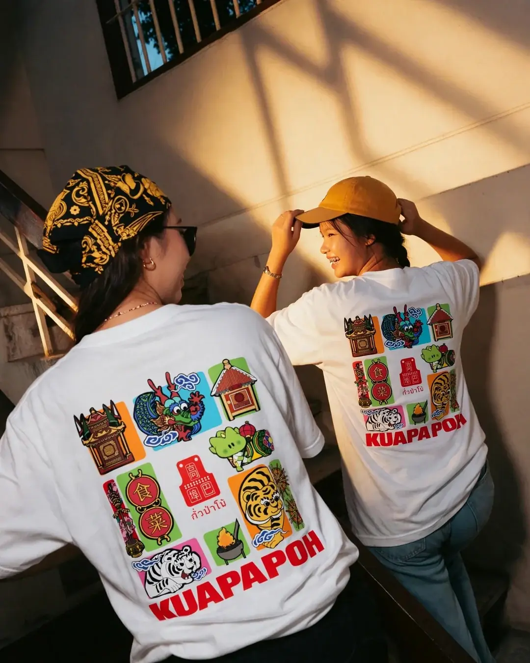 สองเพื่อนใส่เสื้อเทศกาลกินผักกั่วป่าโพ้ หันหลังโชว์ลายในบันไดแสงเย็น